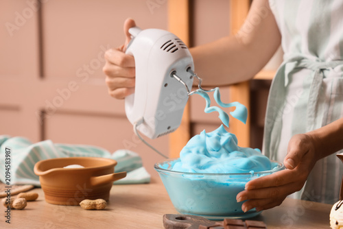 Принти на полотні Woman whipping blue egg whites with mixer in kitchen, closeup