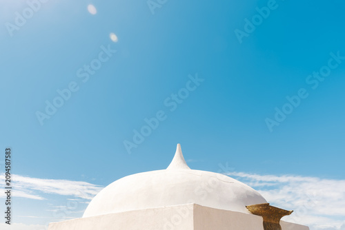 Close up architectural shot of a clean white plastered dome building with a pointed spire against a clear blue sky. Stock photo