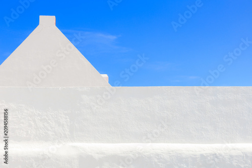 Clean low angle shot of a white geometric building edge and chimney structure isolated against a bright blue sky. Stock photo