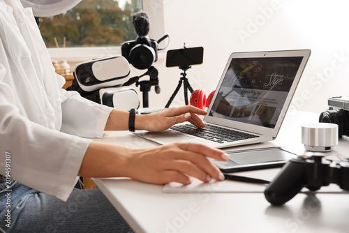 Female blogger using laptop with modern gadgets at table, closeup