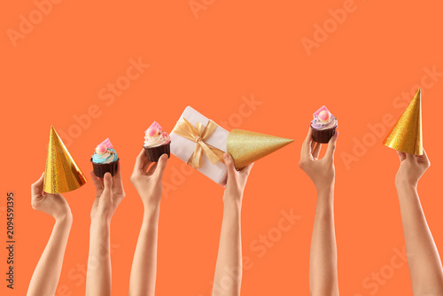 Foto Many female hands with birthday cupcakes, gift box and party hats on orange back
