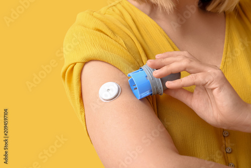 Foto Woman with glucose sensor for measuring blood sugar level and applicator on yellow background, closeup