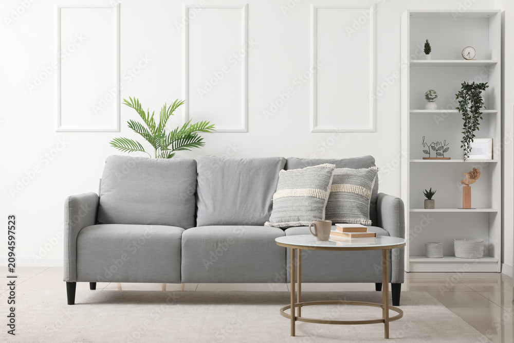 Fototapeta premium Interior of light living room with grey sofa, table and shelf unit