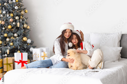 Young lesbian couple with dog hugging in bedroom on Christmas eve