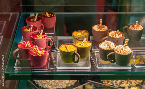 Hot chocolate drinks topped with whipped cream sprinkles and wafer stick arranged in a display case