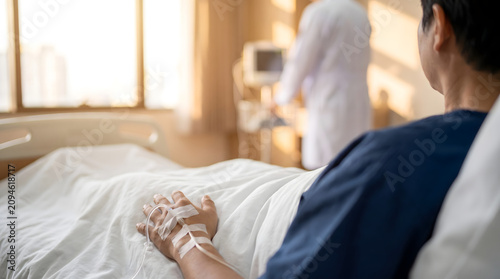 Senior patient lying in hospital bed with IV line attached to hand during medical checkup with blurred physician