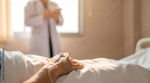Sick patient resting in medical clinic bed with IV drip on hand during professional doctor checkup consultation