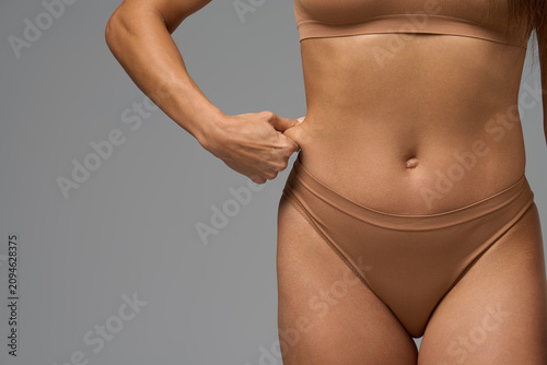 Fit woman in beige underwear gently pinching skin on waist showing real body