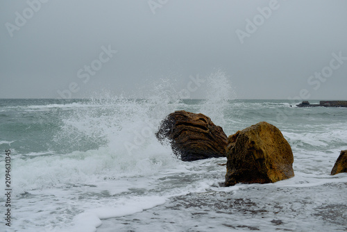 Large stones on the seashore, against which waves break during a storm.