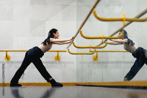 Tableau sur toile Dancer stretches at the ballet barre in a studio while looking at her reflection