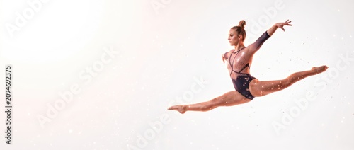 Young woman in mid-air gymnastics leap on white background