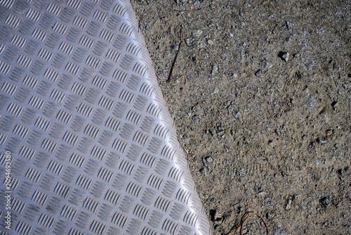 Industrial aluminum tread plate meeting rough gravel ground texture.