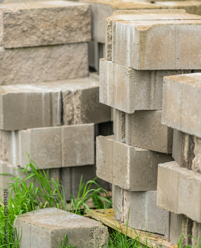 Stacked concrete paving blocks stored outdoors in grass.