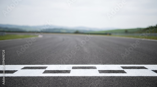 Close-up of a checkered finish line painted on an empty asphalt racing circuit with blurred hills background