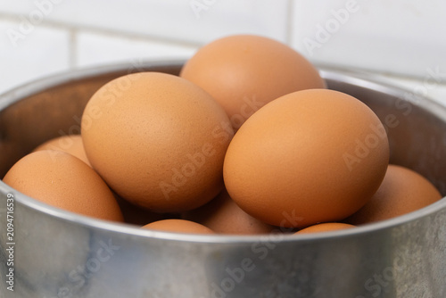 Brown chicken eggs in metal bowl on kitchen counter