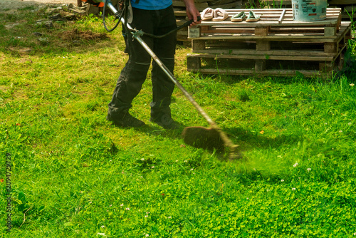 Man using a weed trimmer to cut grass in a yard during daytime