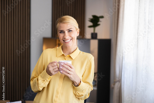 Smiling blond woman holding a coffee cup, relaxing during a break in an office or home environment