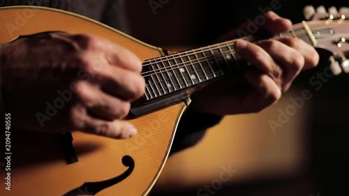 Close-up of hands playing a mandolin, intricate fingerwork on strings, warm lighting