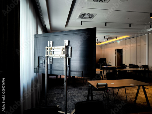 Back view of large flat screen monitor with wall mount bracket in modern Munich conference room, presentation technology setup near window and curtains, business meeting equipment and AV installation 