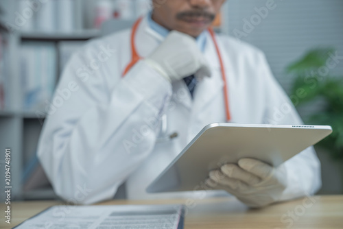 Middle Eastern male doctor with mustache reviewing patient records on a digital tablet in a modern clinic. Professional healthcare consultation, electronic medical records and telemedicine concept.