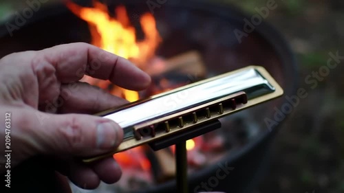 Close-up of hands playing harmonica by a campfire, outdoor leisure and music