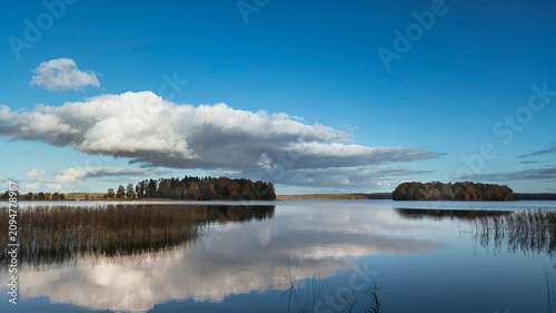 Tableau sur toile Perfect mirror reflection of scenic forest lake with clouds under clear blue sky