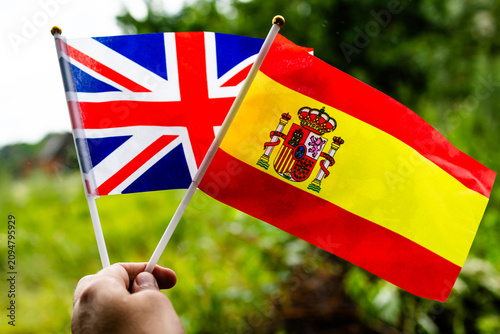 Cheerful miniature flags from the United Kingdom and Spain fly together in nature representing positive diplomacy cultural discovery sports enthusiasm and opportunities for students professionals