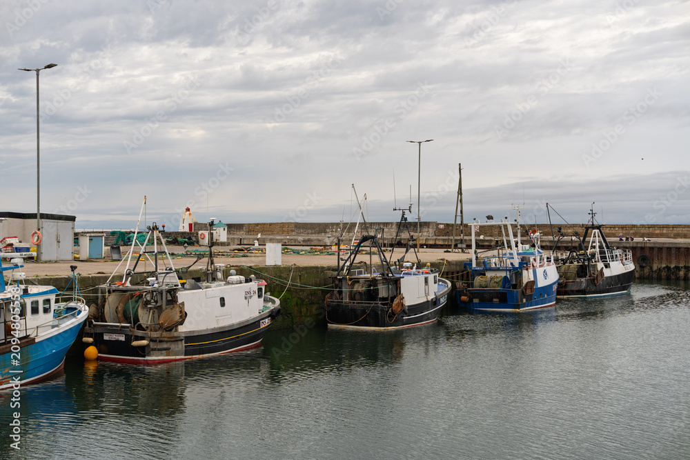 Fototapeta premium Fishing boats moored at Burghead Harbor in Moray, Scotland, under an overcast sky