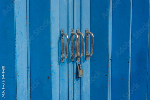 Obraz na plátně A blue metal sliding door with vertical panels, four parallel silver handles, and a padlock, commonly used for shop security