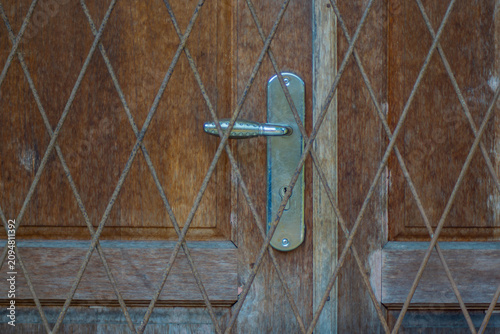 Wooden door with metal handle behind diamond-pattern iron lattice grill