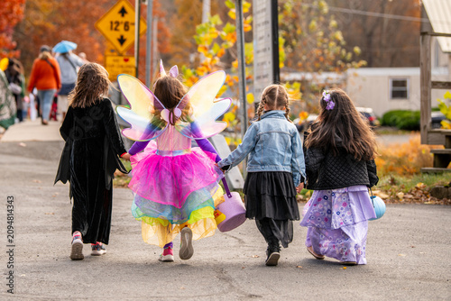 Foto Four children in Halloween costumes walk down a quiet, tree-lined neighborhood street toward trick-or-treating, illustrating friendship, autumn traditions, community, and childhood with no faces