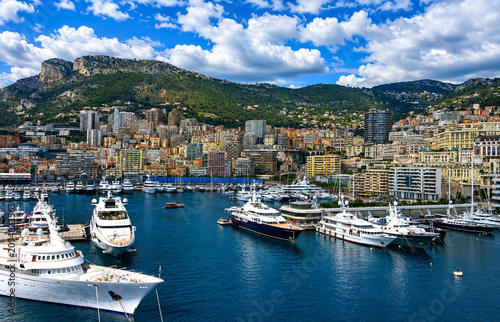 Luxury motor yachts moored in the famous Port Hercule marina in Monte Carlo, Monaco. The waterfront skyline, upscale residences, and surrounding hills showcase one of the world's premier luxury travel
