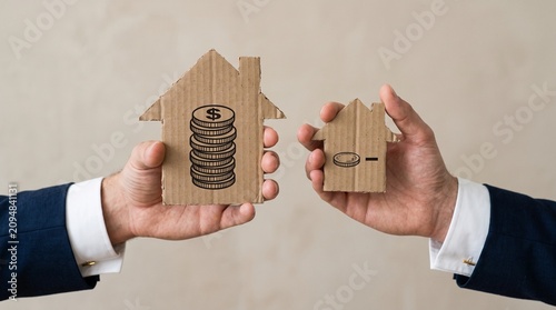 Real estate investment concept with cardboard house icons, hands holding property symbols with money and coin graphics, mortgage and housing market growth