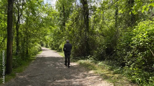 Elderly man walking alone on a path in a lush green forest promoting active aging and mental health awareness.