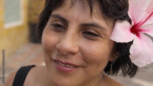 Beautiful middle aged woman with hibiscus flower smiling relaxed at camera celebrating summer style, natural beauty, confidence and feminine clean look