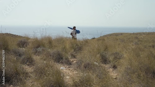Young man hiking on a coastal hill overlooking the Mediterranean sea in the background. Scenic view of vacation time.