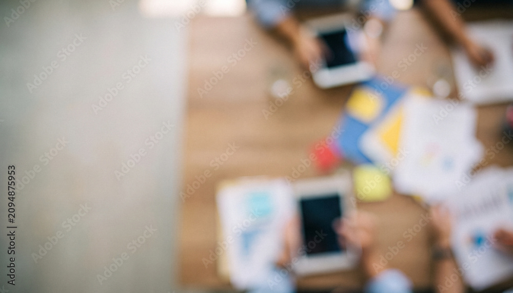 Obraz premium A top-down view of hands interacting with digital devices on a wooden table, surrounded by colorful documents and stationery, illustrating collaboration and technology.