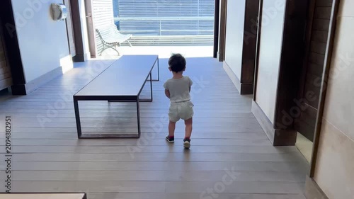 Toddler boy walking alone down a modern hallway
