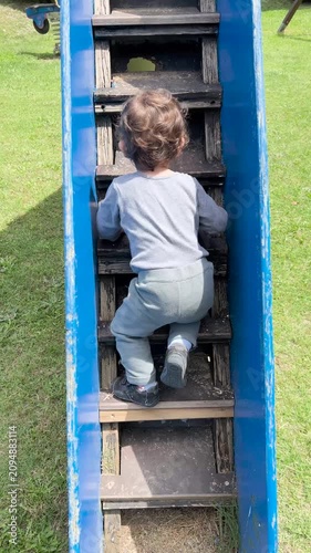 Toddler boy confidently climbing up slide ladder