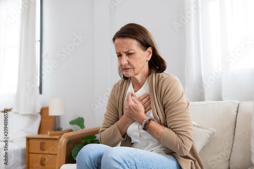 Mature woman holding her chest suffer from heart disease on a couch