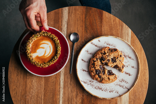 Overhead pistachio coffee with latte art and chocolate cookie on table