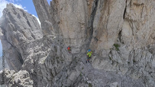 Two hikers crossing the exposed ledge of Via Ferrata Bocchette Centrali beneath Campanile Alto, Brenta Dolomites