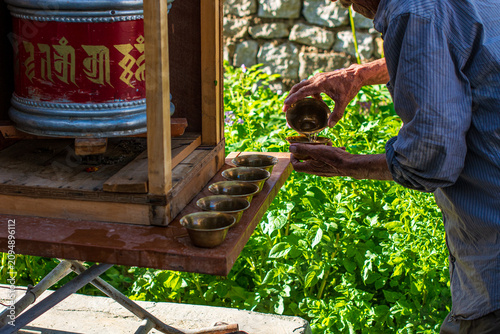 Vászonkép Man pouring water into ritual bowls near a Buddhist prayer wheel, Ladakh
