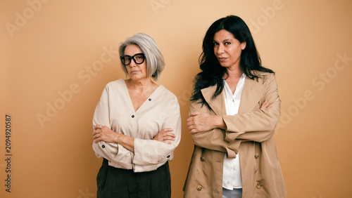 Two mature women standing side by side with crossed arms, expressing confidence, empowerment, and professionalism