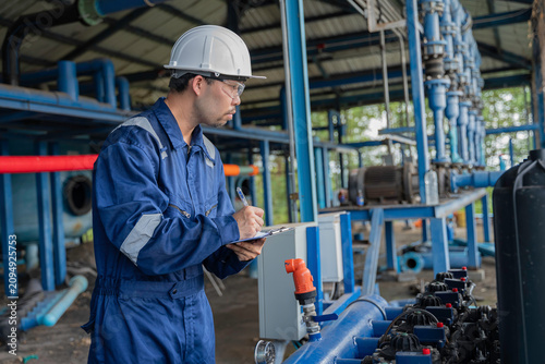 Professional engineer performing maintenance inspection of industrial water filtration system with multiple membrane units. Technician recording operational data for water treatment facility process.
