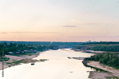 Bild auf Leinwand Expansive river landscape with distant city skyline and sandy shores at sunset