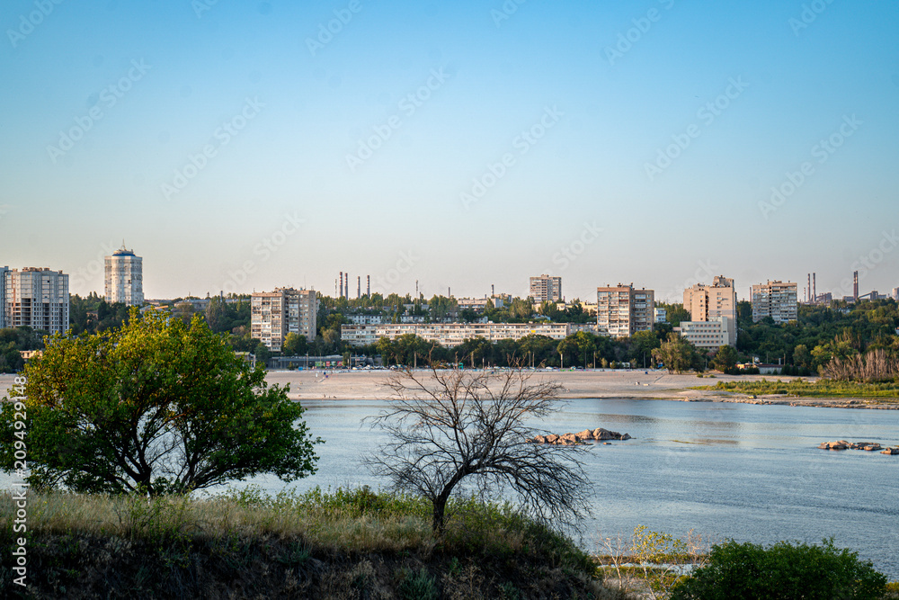 Fototapeta premium Panoramic view of a riverside city skyline with apartment buildings and green trees