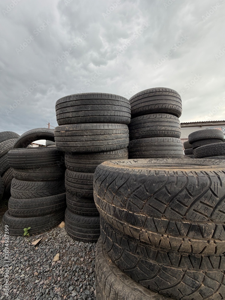 Obraz premium Pile of used tires and second hand car tyres. Old black rubber tyre waste for recycle, landfill or sale at manufacturing yard background for automotive industry and environmental concept.