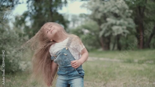 Cute little girl with very long hair spinning and shaking her hair in summer park