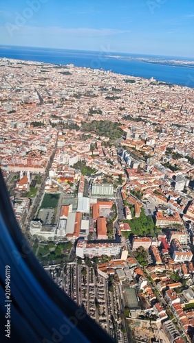 Aerial view of urban landscape featuring residential buildings, green parks, and coastal area with blue ocean in the background under clear sky